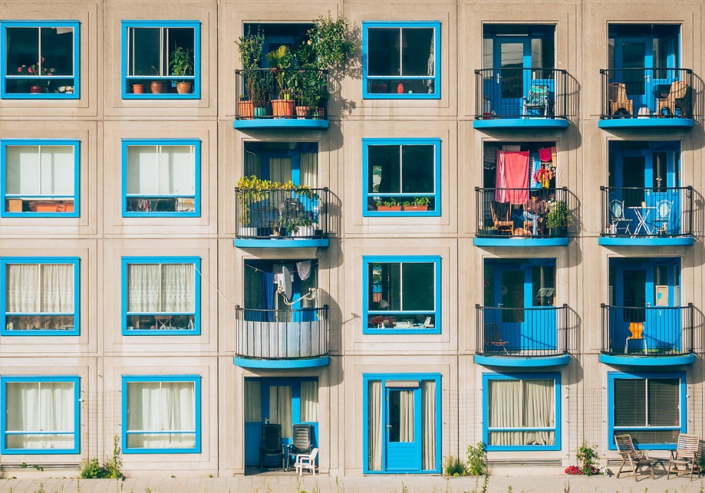 Facciata di un edificio residenziale con balconi e finestre blu, piante e panni stesi.