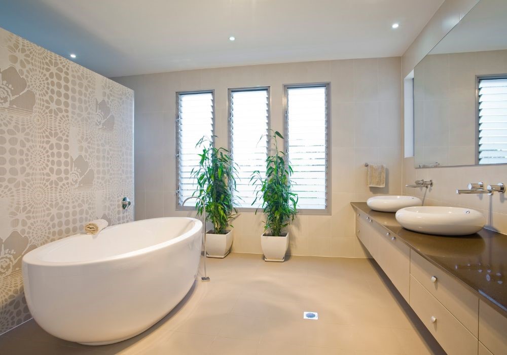 Bagno moderno con vasca ovale, doppio lavabo, piante e finestre con persiane.