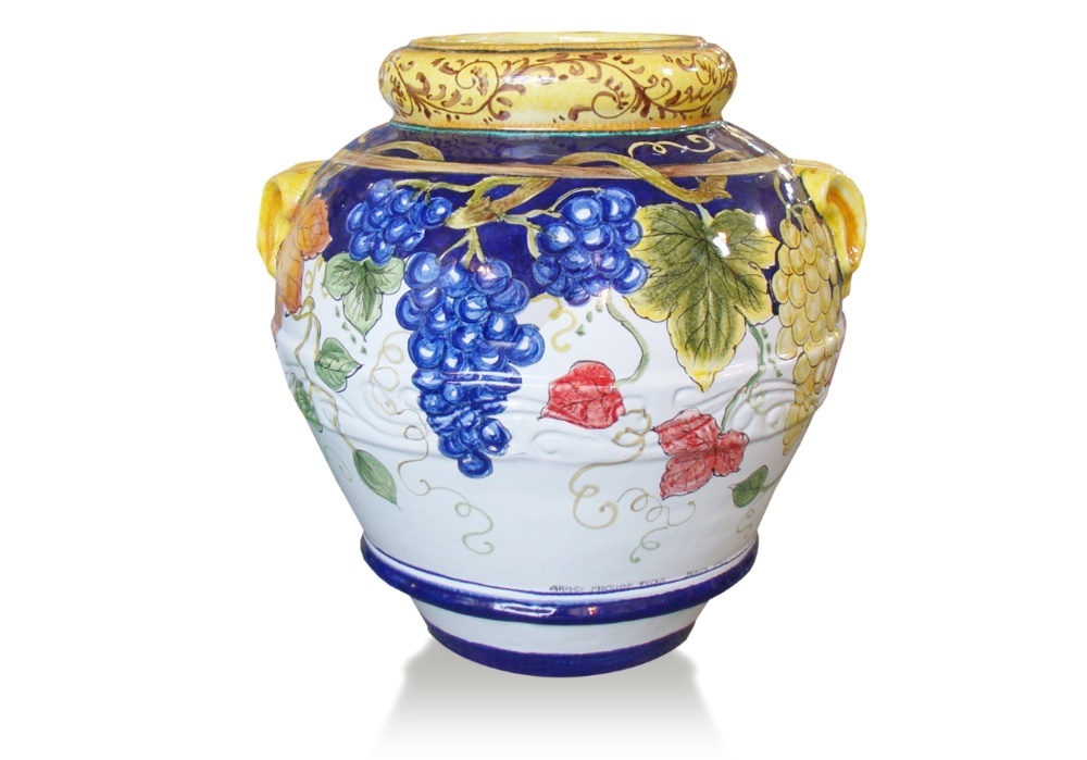 Vaso in ceramica dipinto a mano con grappoli d'uva blu e gialli, foglie verdi e fiori rossi su sfondo bianco.