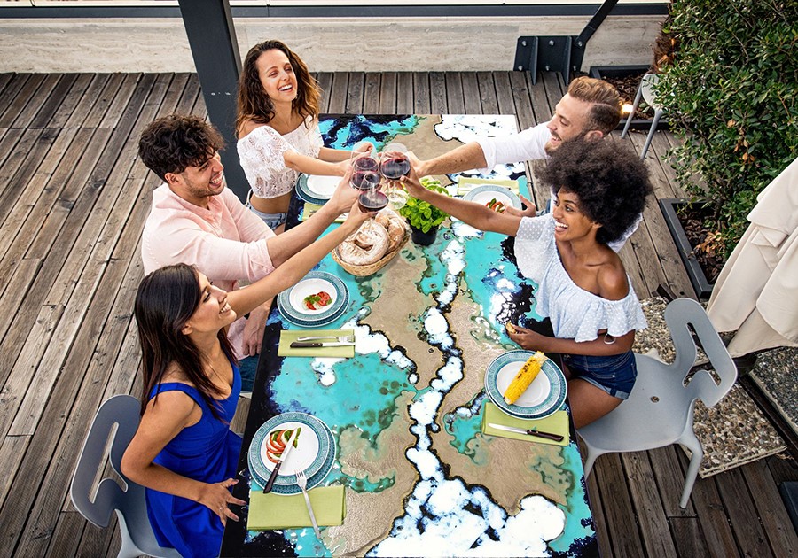 Amici sorridenti brindano con vino rosso a un tavolo da pranzo artistico su una terrazza in legno.