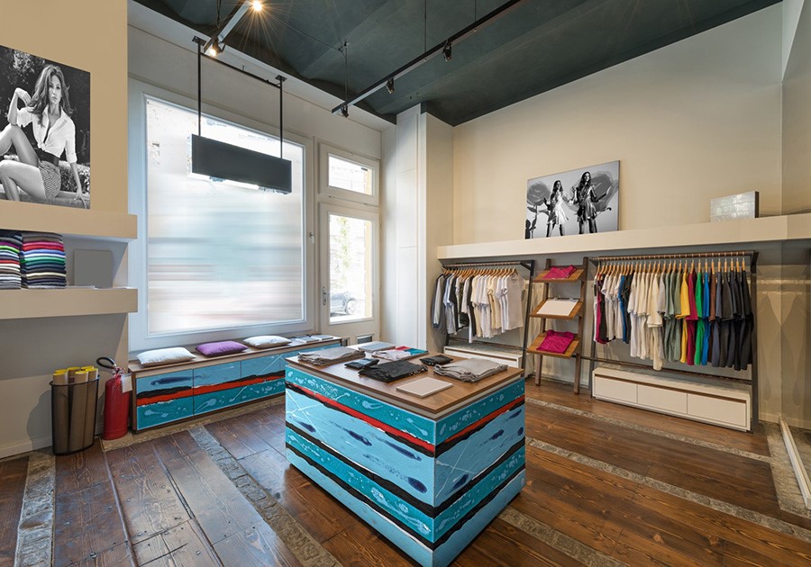 Interno di un negozio di abbigliamento moderno con vestiti esposti, un bancone centrale e poster alle pareti.