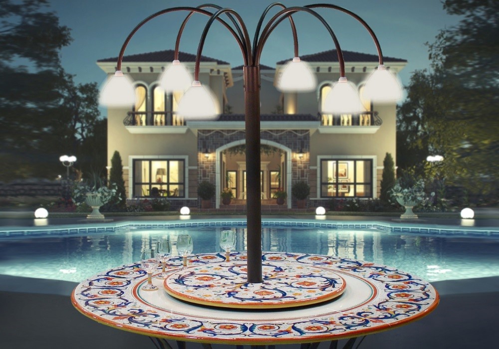 Tavolo esterno con lampade, piscina e villa di lusso sullo sfondo, notte.