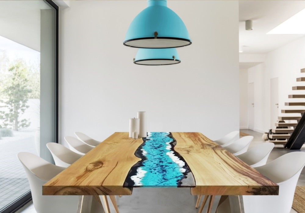 Tavolo in legno con resina epossidica blu, sedie bianche, lampade turchesi in una sala da pranzo moderna.