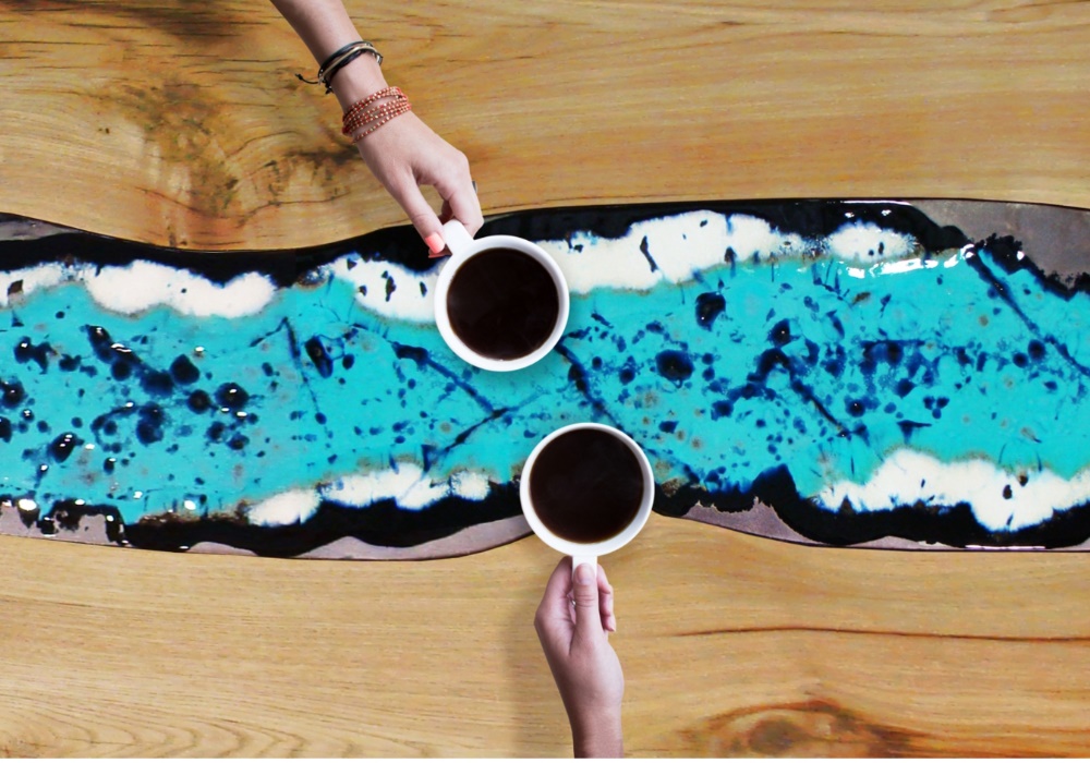 Due mani tengono tazze di caffè su un tavolo in legno con un inserto decorativo blu e nero.