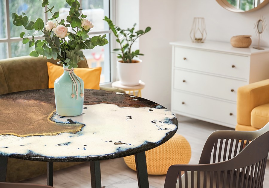 Tavolo rotondo con vaso di fiori, sedie e cassettiera bianca in un soggiorno luminoso.