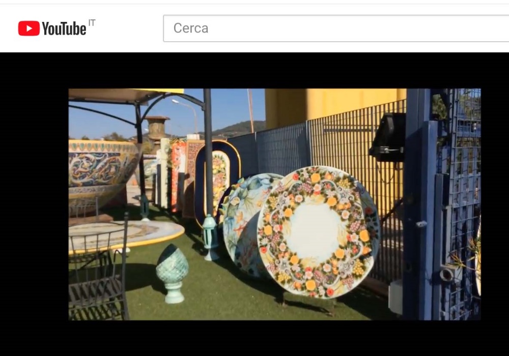Grandi piatti decorati e ceramiche artistiche esposti all'aperto, con tavoli e sedie in ferro battuto.