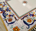 Tavolo in ceramica dipinta a mano con motivi floreali e arabeschi blu, arancioni e verdi su sfondo bianco craquelé.