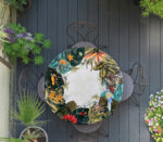 Tavolo rotondo con motivo tropicale di foglie e fiori colorati su un patio in legno scuro con piante.