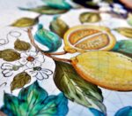 Dettaglio di ceramica dipinta a mano con limoni gialli, foglie verdi e fiori bianchi, stile mediterraneo.