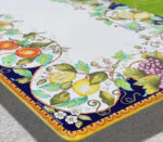 Tavolo in ceramica dipinto a mano con limoni, arance, uva e fiori su sfondo bianco e bordo blu e giallo.