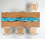 Tavolo in legno con intarsio in resina blu e bianca che simula un fiume, con quattro sedie in legno chiaro.