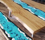 Tavolo in legno massello con resina epossidica turchese che simula un fiume, design moderno e artigianale.