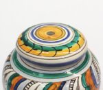 Coperchio e bordo di un vaso in ceramica dipinto a mano con motivi geometrici e floreali colorati.