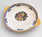 Piatto da portata in ceramica bianca con bordo giallo e blu, decorato con un grappolo di frutta al centro.